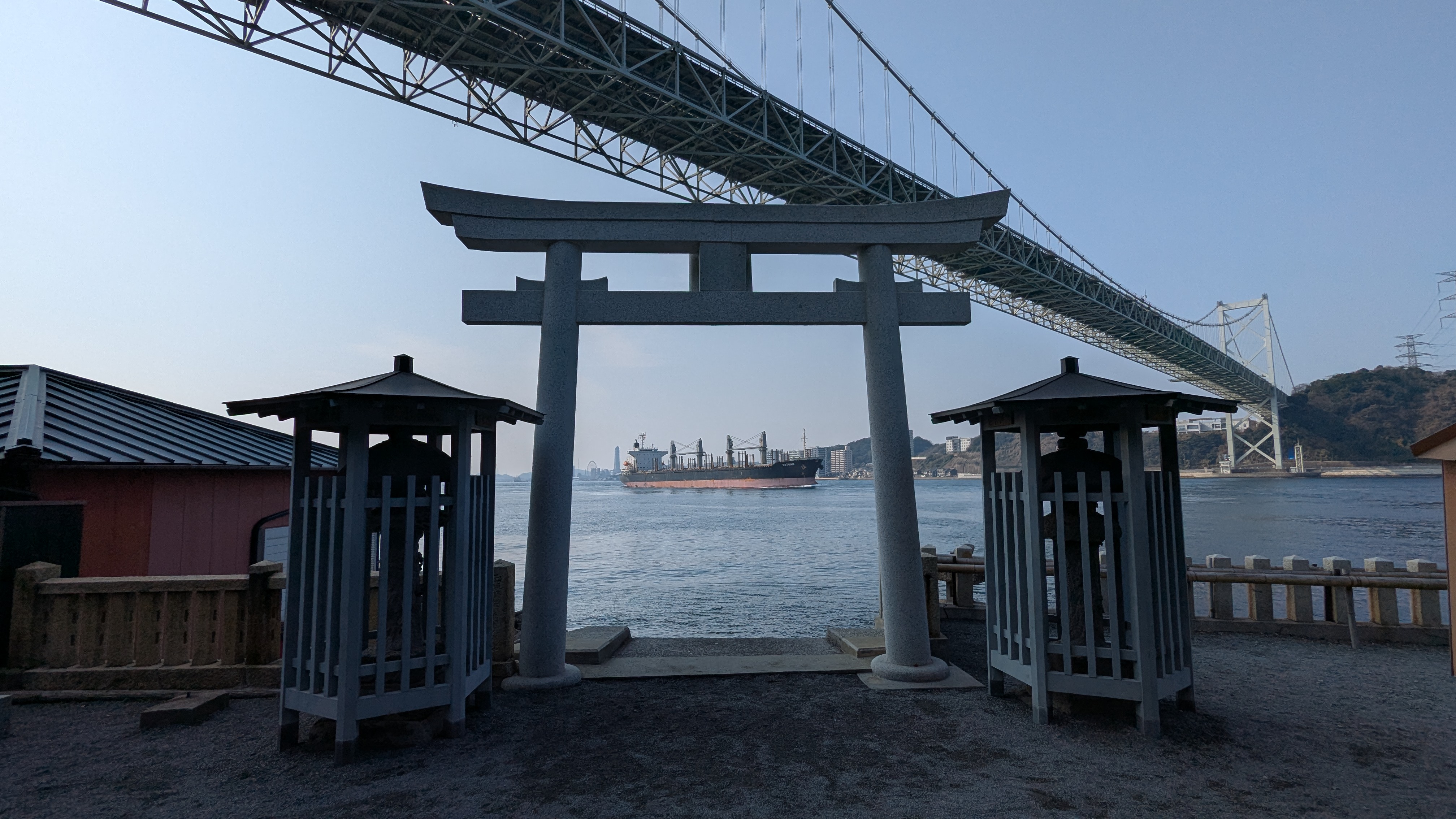 Cargo ship passing under Kanmon Bridge seen through Torii gate at Mekari Shrine, Japan maritime photography